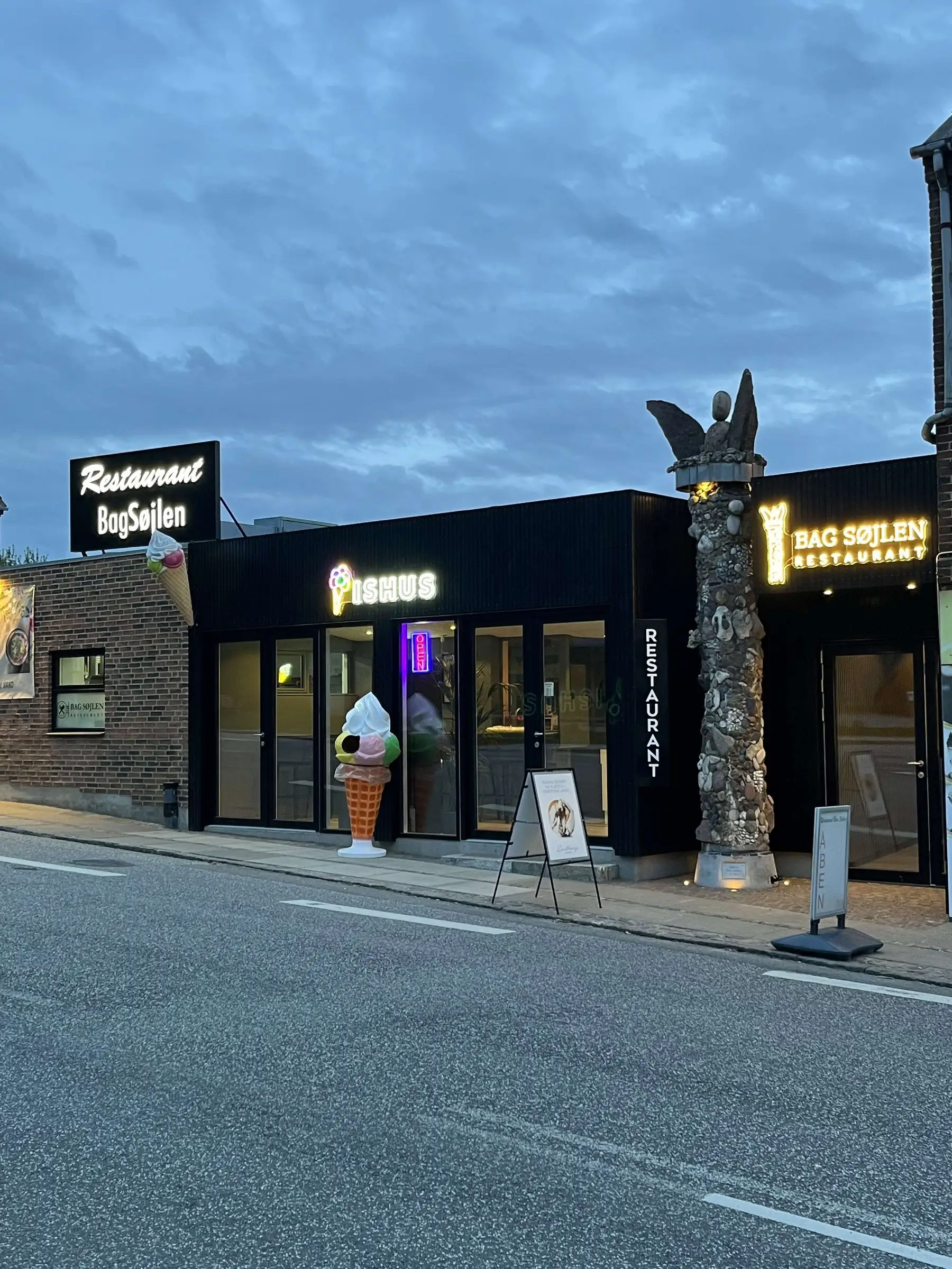 Facaden på Hovedgaden med søjlen, restaurantens skilt og ishuset i aftenlys