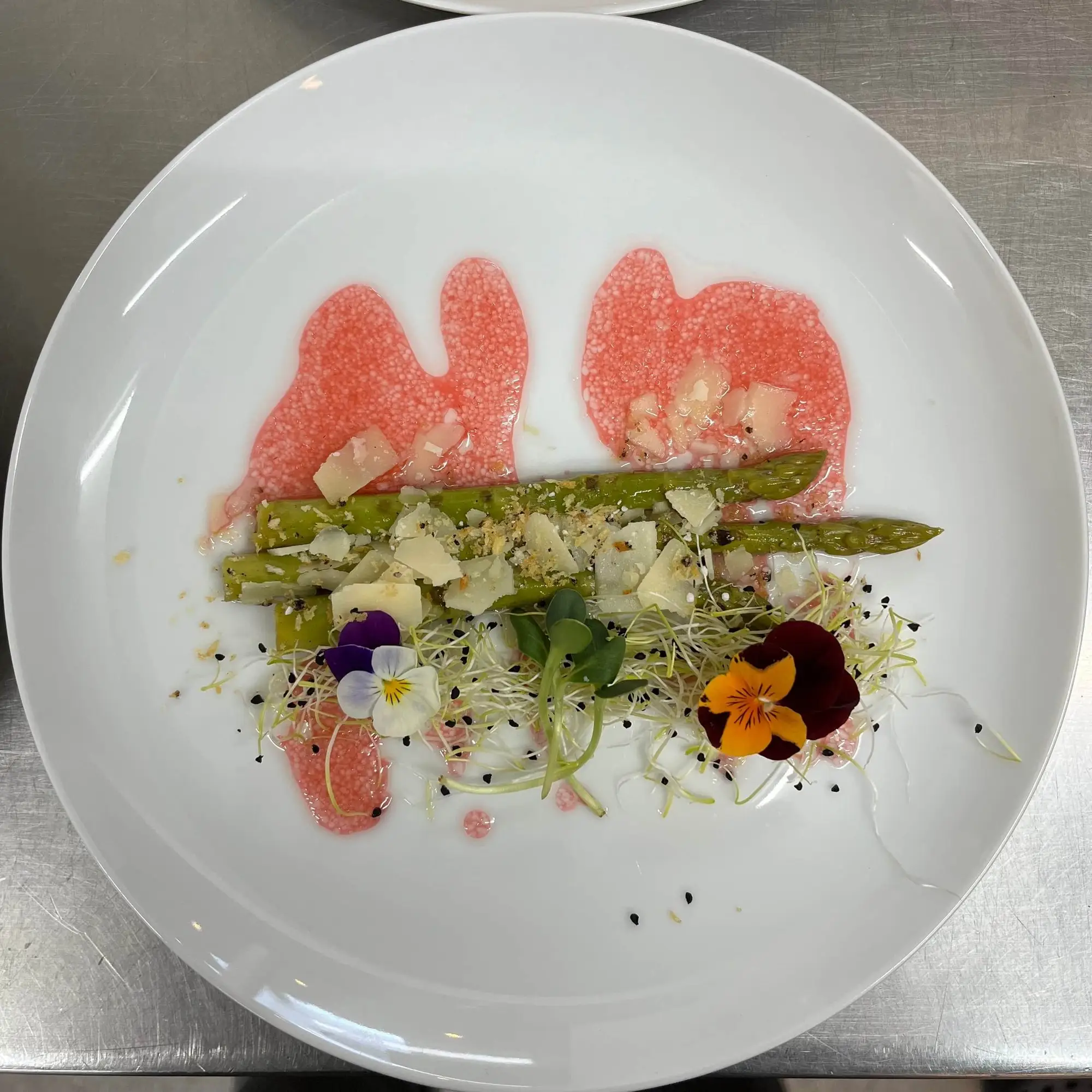 Sæsonret med asparges, melon og spiselige blomster på en hvid tallerken