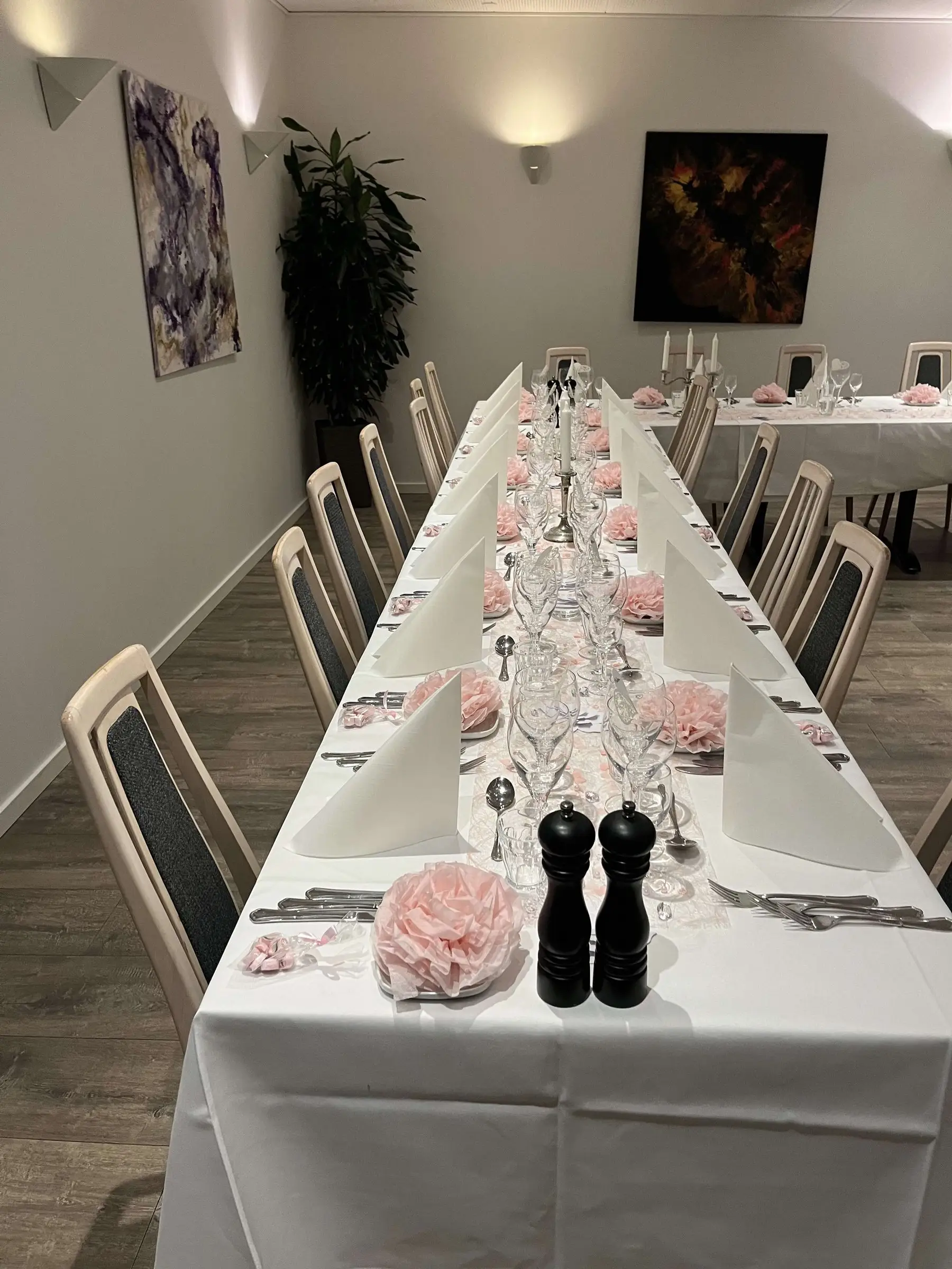 Langbord dækket til fest i selskabslokalet med lyserøde blomster